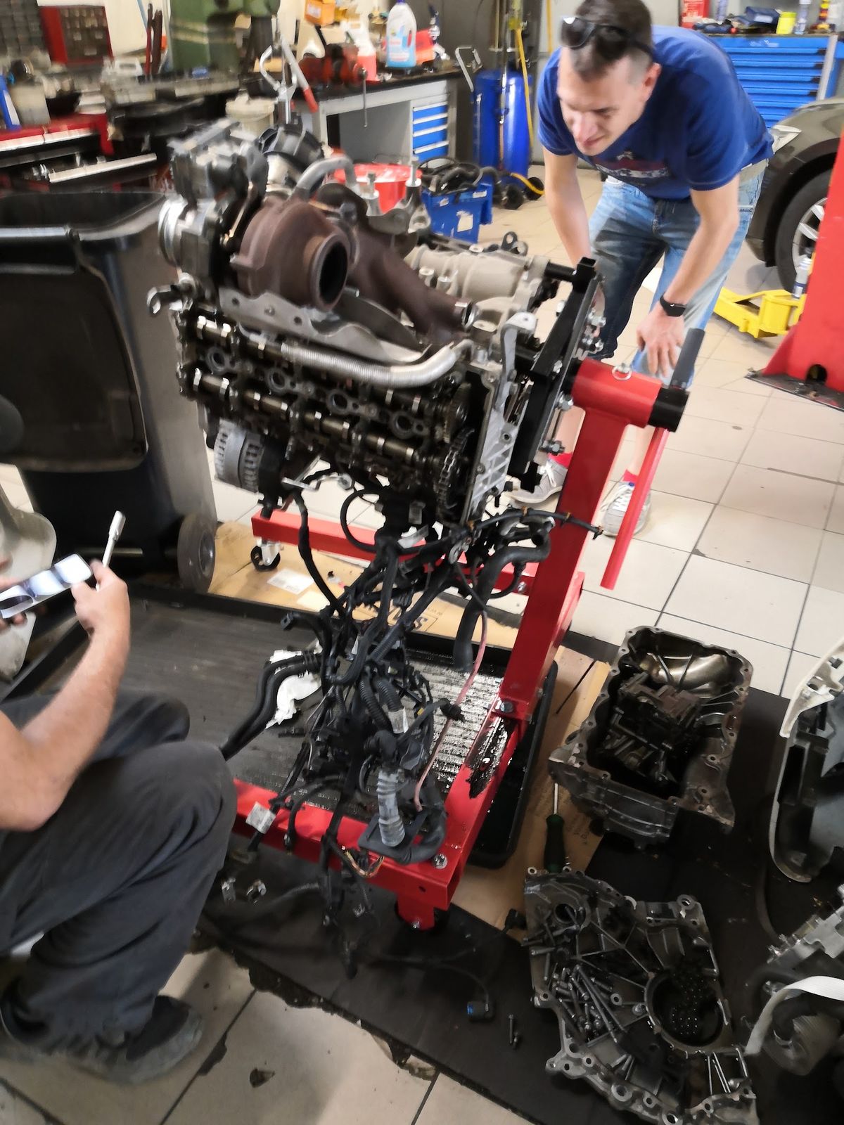Motor vybratý z auta na červenom montážnom stojane v dielni Boxer servis, pri ňom mechanik