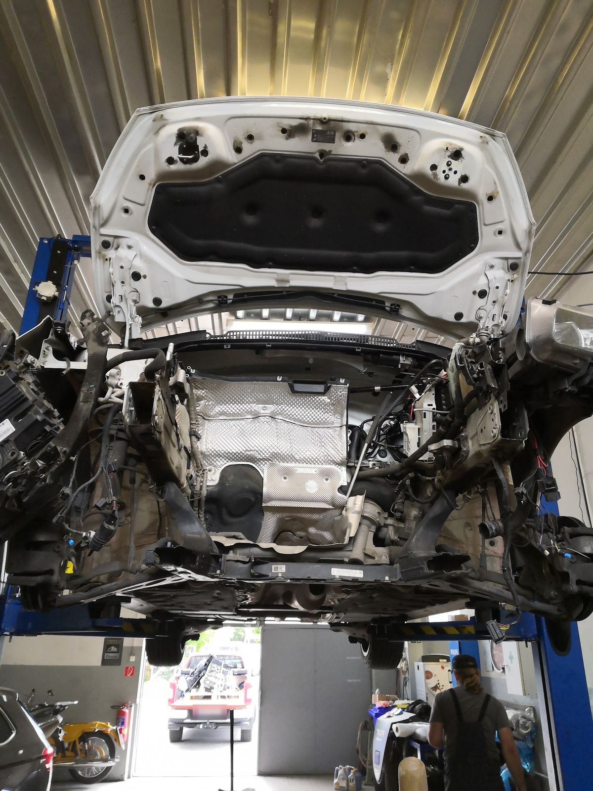 Auto na zdviháku s vybratým motorom, v pozadí motocykle a otvorená brána dielne